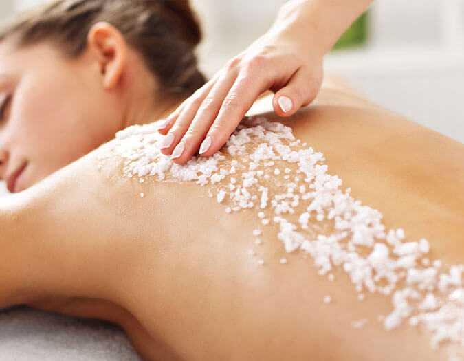 Hands applying body scrub on woman's back