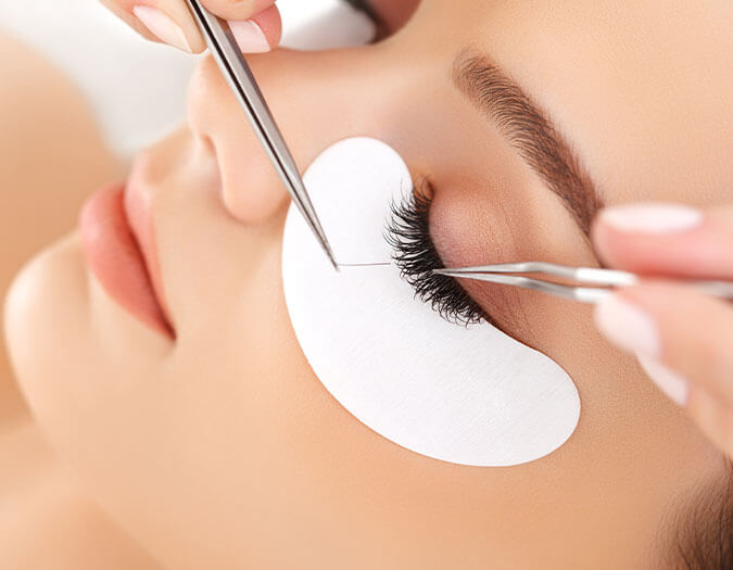 Hands applying an eyelash extension in a woman's eye