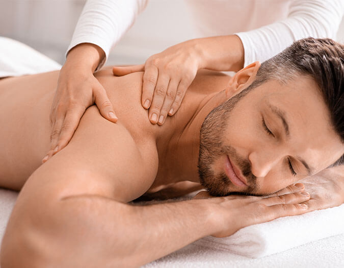 Men lying on a white bed, having a back massage