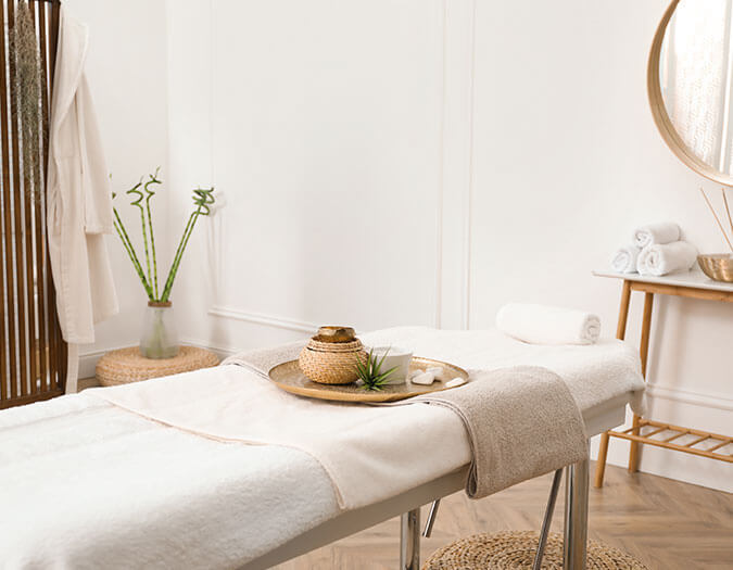 White, relaxing, and cozy massage room with bed, candles and towels.