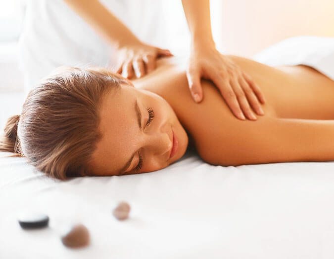 Woman laying on white bed, having a relaxing massage on her back