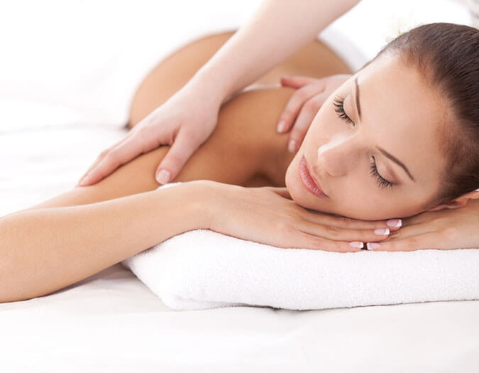 Woman lying on a white bed, having a relaxing massage on her back